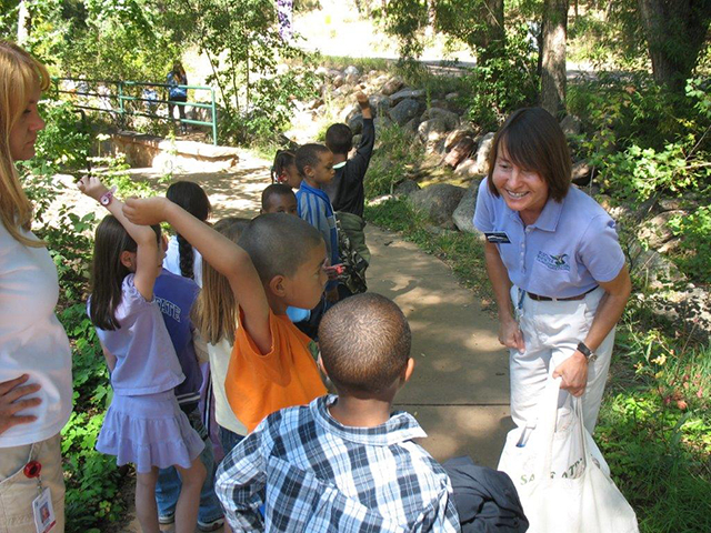 woman teaching a group of children outside along bank of creek