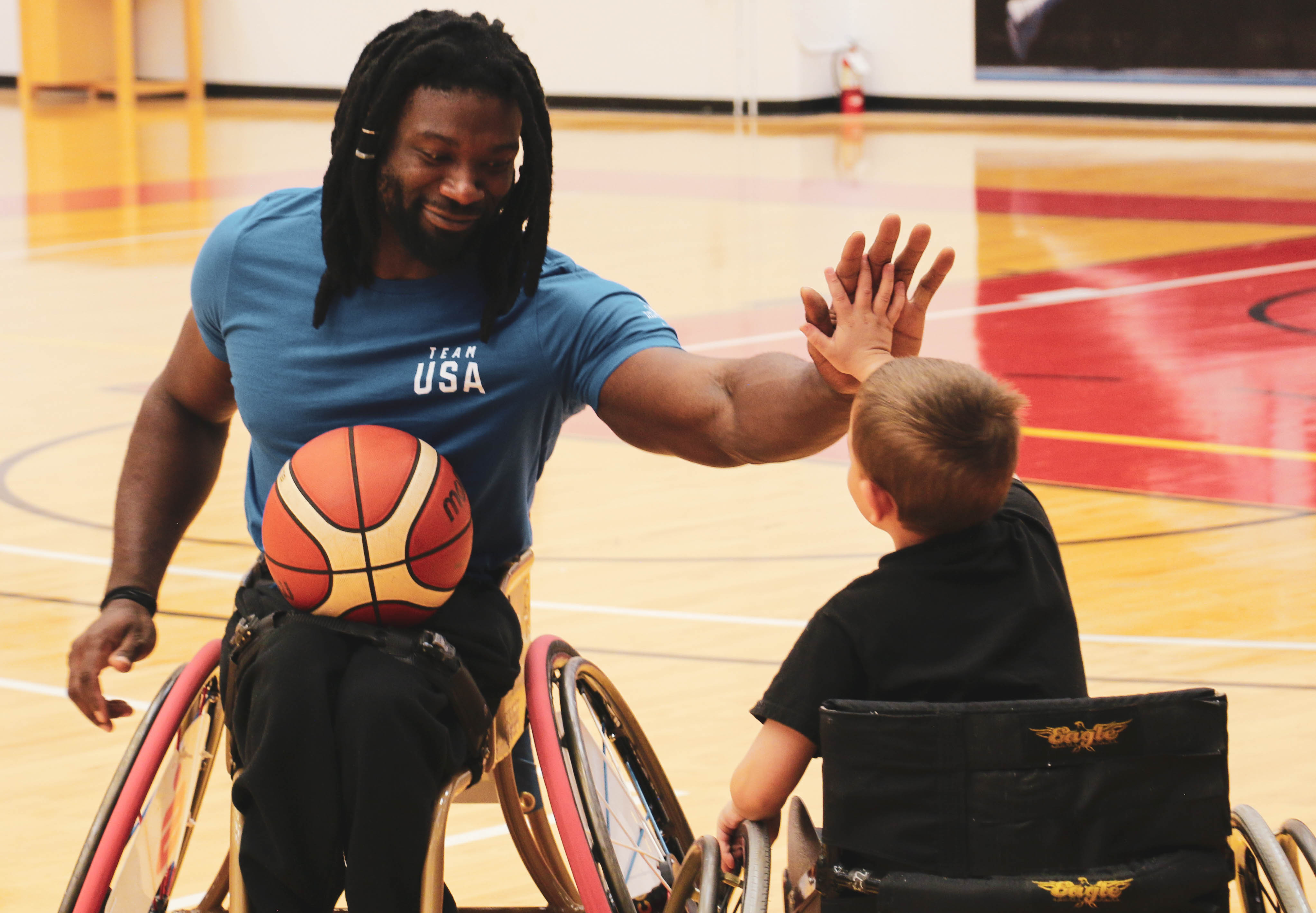 An athlete in a wheelchair, and a young boy in a wheelchair high five