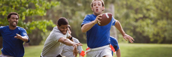 man with football running. Man running behind him lunges for flag