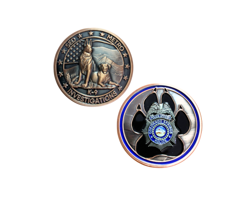 A picture of the CSPD K9 Coin, it's bronze featuring two dogs in front of the american flag and mountains and the back has a large black paw print and the CSPD badge with a blue circle around it.
