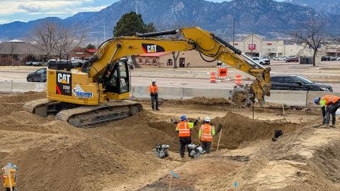 An excavator digs a trench for a waterline on South Academy Blvd.