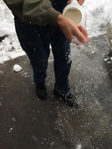 person sprinkling deicer on a driveway 