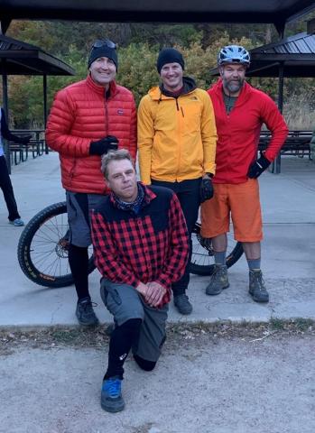 four people pose with a bike. Three people are wearing red and one is wearing yellow.