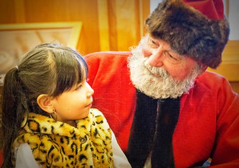little girl and santa look at each other as girl sits on his lap.