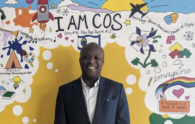 Mayor Yemi in front of a sign that says "I am COS"
