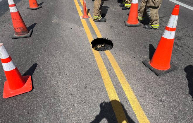 A small sinkhole with workers around it repairing it.