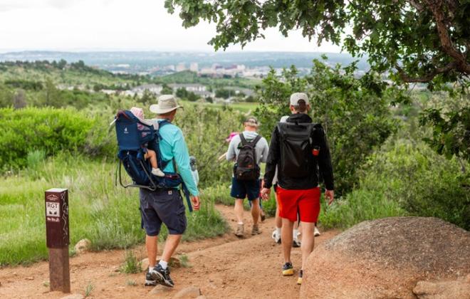Residents hike on a trail through green vegetation in a park on a summer day.