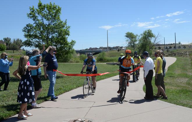 A group of bike riders break through a red ribbon stretched across the new bike path