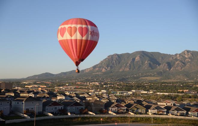 red hot air balloon hovering over neighborhood. Cheyenne Mountain in the background.