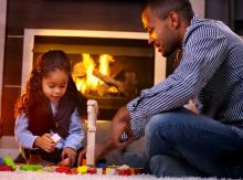 A little girl and her dad play with blocks in front of the fireplace